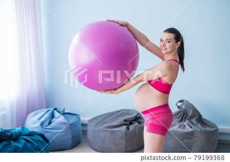 A pregnant woman in sportswear is doing gymnastics for pregnant women. The girl is engaged in fitness with a ball for expectant mothers. Last trimester. A pregnant woman in sportswear is doing gymnastics for pregnant women. The girl is engaged in fitness with a ball for expectant mothers. Last trimester. 79199368
