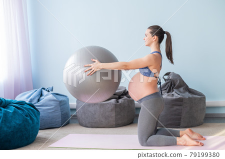 Pregnant caucasian woman on fitness with a ball. Yoga for expectant mothers. Girl in the classroom in preparation for childbirth. Pilates in the last trimester. 79199380