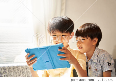 兩個男孩盯著客廳裡的平板電腦屏幕 79199720