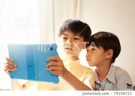 兩個男孩盯著客廳裡的平板電腦屏幕 兩個男孩盯著客廳裡的平板電腦屏幕 79199721
