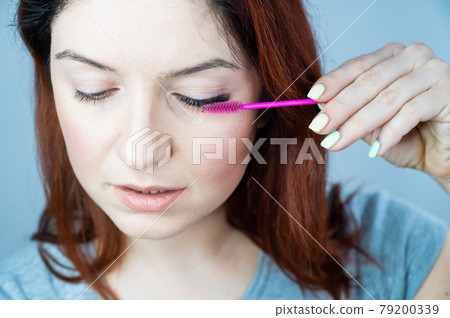 Red head woman brushing her extension eyelashes with a brush. girl with impending eyelid make-up mascara. Beauty industry. Red head woman brushing her extension eyelashes with a brush. girl with impending eyelid make-up mascara. Beauty industry. 79200339