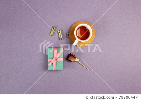 Gift box, cup of tea, wooden clip, dry rose flower on purple background. flat lay, top view, copy space 79200447