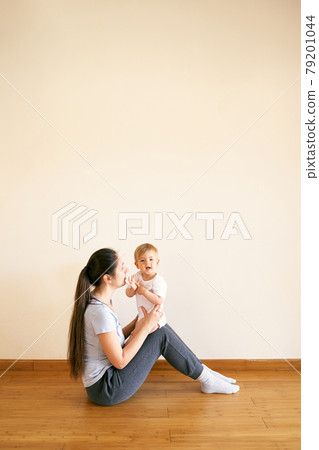 Mom sitting on the floor and holding her baby on her lap Mom sitting on the floor and holding her baby on her lap 79201044