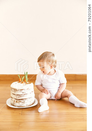 Little girl sitting on the floor in the room and looking at the carrot cake Little girl sitting on the floor in the room and looking at the carrot cake 79201064