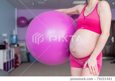 Cropped view of unrecognizable pregnant woman in yoga class. Future mother faceless with a bare tummy is engaged in fitness with a ball. 79201481