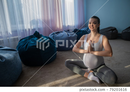 Pregnant woman smiles in yoga practice. A woman in the third trimester leads Pilates. Classes to prepare for childbirth. Waiting for the baby. Namaste Pregnant woman smiles in yoga practice. A woman in the third trimester leads Pilates. Classes to prepare for childbirth. Waiting for the baby. Namaste 79201616