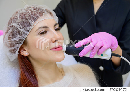 Portrait of a middle-aged woman receiving a non-surgical rejuvenation procedure at a cosmetologist. RF face lifting. Hardware facial massage. Portrait of a middle-aged woman receiving a non-surgical rejuvenation procedure at a cosmetologist. RF face lifting. Hardware facial massage. 79201672