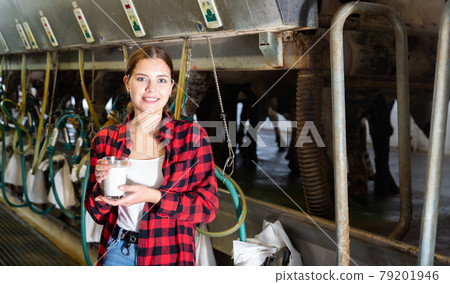 Female milker posing with glass of milk on dairy farm Female milker posing with glass of milk on dairy farm 79201946