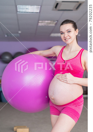A pregnant woman in sportswear is doing gymnastics for pregnant women. The girl is engaged in fitness with a ball for expectant mothers. Last trimester. 79202235
