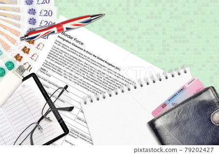 English form Immigration clearance to enter the UK from Border force services lies on table with office items. UK rborder force paperwork 79202427
