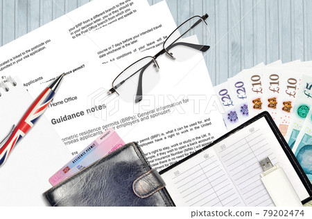 English form BRP with guidance notes to applying biometric residence permit card from UK visas and immigration services lies on table with office items. UK residence permit paperwork English form BRP with guidance notes to applying biometric residence permit card from UK visas and immigration services lies on table with office items. UK residence permit paperwork 79202474