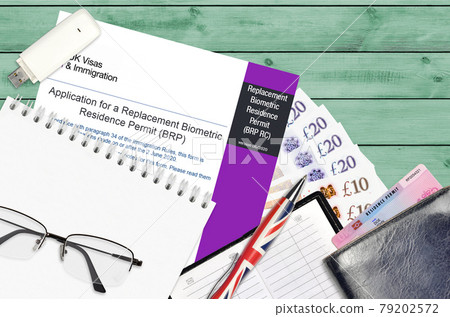 English form BRP RC Application for a replacement biometric residence permit card from UK visas and immigration services lies on table with office items. UK residence permit paperwork 79202572