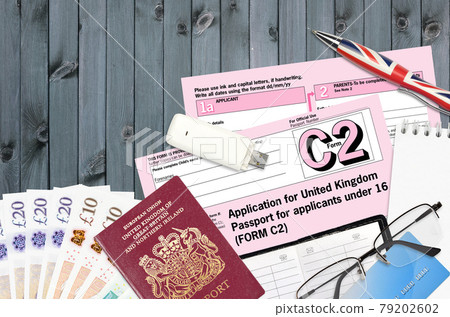 English form C2 Application for United Kingdom passport for applicants under 16 lies on table with office items. UK passport paperwork English form C2 Application for United Kingdom passport for applicants under 16 lies on table with office items. UK passport paperwork 79202602