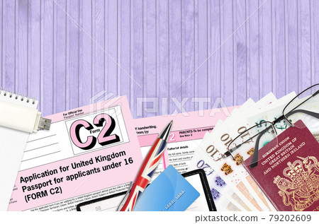 English form C2 Application for United Kingdom passport for applicants under 16 lies on table with office items. UK passport paperwork 79202609