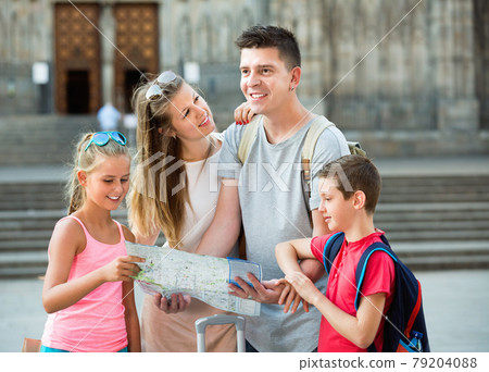 Parents with two kids traveling together searching location on paper map 79204088