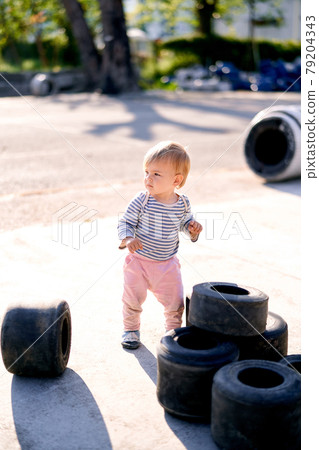 Kid stands near the piled up car tires in the parking lot Kid stands near the piled up car tires in the parking lot 79204343