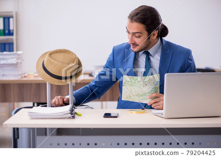 Young male employee preparing for trip in the office Young male employee preparing for trip in the office 79204425