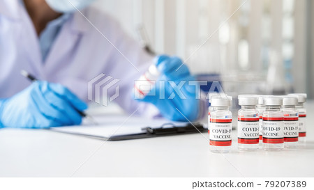 Covid-19 coronavirus vaccine bottles on white table with scientist working in pharmaceutical research laboratory background. Fight against Covid-19 coronavirus Concept. Covid-19 coronavirus vaccine bottles on white table with scientist working in pharmaceutical research laboratory background. Fight against Covid-19 coronavirus Concept. 79207389