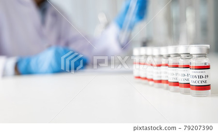 Covid-19 coronavirus vaccine bottles on white table with scientist working in pharmaceutical research laboratory background. Fight against Covid-19 coronavirus Concept. Covid-19 coronavirus vaccine bottles on white table with scientist working in pharmaceutical research laboratory background. Fight against Covid-19 coronavirus Concept. 79207390