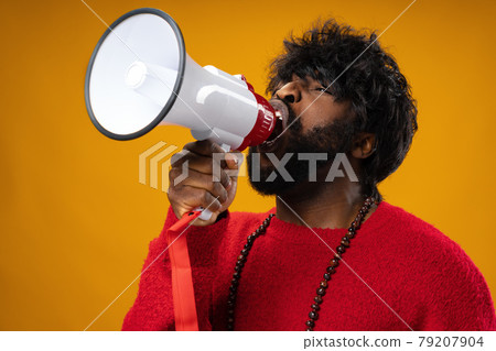 Young african american man in red hoodie screaming in megaphone against yellow background Young african american man in red hoodie screaming in megaphone against yellow background 79207904