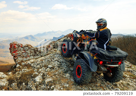Man in helmet sitting on ATV quad bike in mountains 79209119