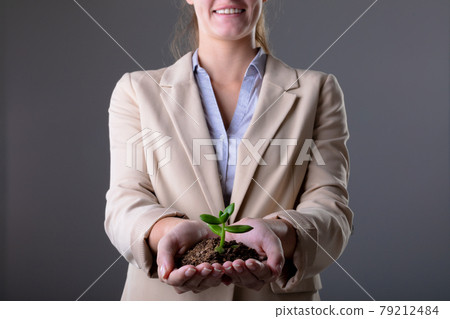 Smiling caucasian businessman holding plant seedling, isolated on grey background 79212484