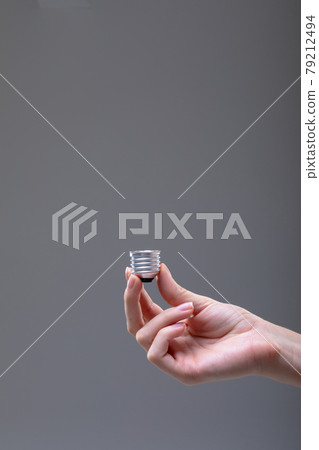 Close up of caucasian businesswoman holding base of light bulb, isolated on grey background 79212494