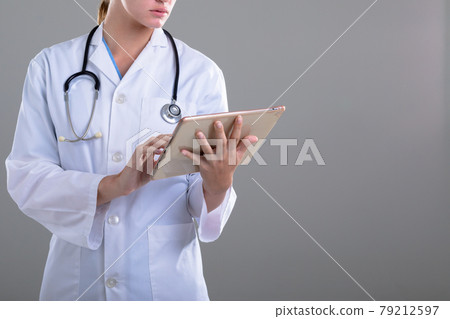 Midsection of caucasian female doctor using tablet, isolated on grey background 79212597