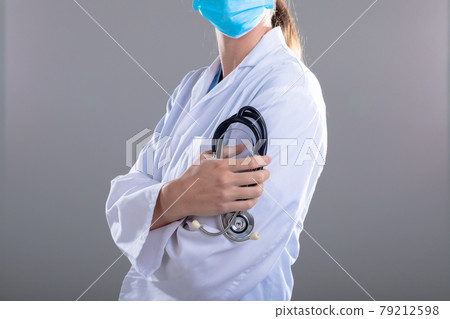 Caucasian female doctor wearing face mask holding stethoscope 79212598