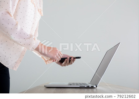 Midsection of caucasian businesswoman using laptop and smartphone, isolated on grey background 79212602