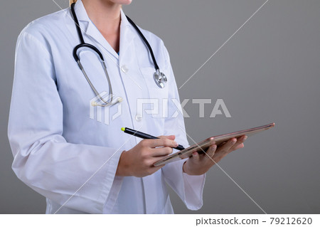 Midsection of caucasian female doctor using tablet, isolated on grey background 79212620