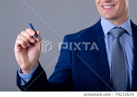Smiling caucasian businessman holding pen, isolated on grey background 79212629