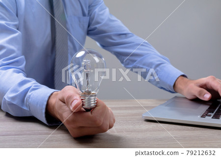 Midsection of caucasian businessman holding light bulb using laptop, isolated on grey background 79212632
