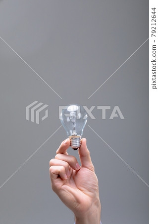 Close up of caucasian businessman holding light bulb, isolated on grey background 79212644