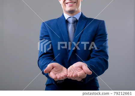 Smiling caucasian businessman showing his hands, isolated on grey background 79212661