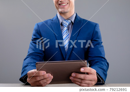 Smiling caucasian businessman using tablet, isolated on grey background 79212691