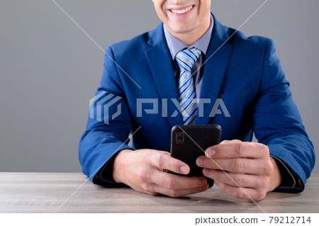 Smiling caucasian businessman using smartphone, isolated on grey background 79212714