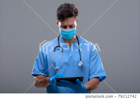 Caucasian male doctor wearing face mask using tablet 79212742