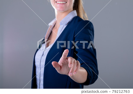 Smiling caucasian businesswoman touching virtual interface, isolated on grey background 79212763