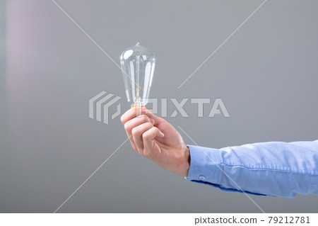Midsection of caucasian businessman holding light bulb, isolated on grey background 79212781