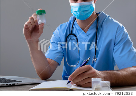 Caucasian male doctor wearing face mask holding box of pills 79212828