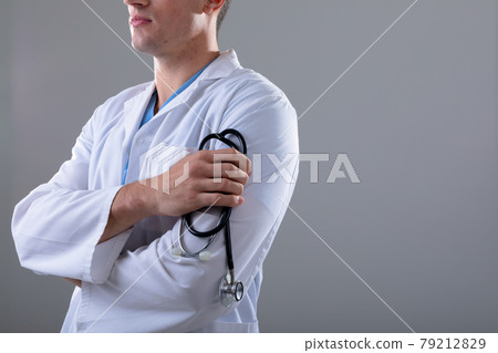 Midsection of caucasian male doctor holding stethoscope, isolated on grey background 79212829