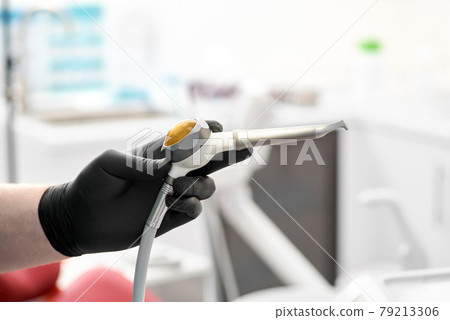 The gloved hand of the dentist holds the Airflow whitening and cleaning brush to remove tartar and plaque. The gloved hand of the dentist holds the Airflow whitening and cleaning brush to remove tartar and plaque. 79213306