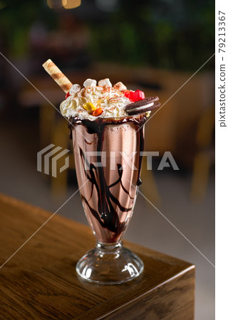 Delicious chocolate shake with chocolate icing and biscuits, marshmallows and candy inside the beautiful interior of modern cafe. Delicious chocolate shake with chocolate icing and biscuits, marshmallows and candy inside the beautiful interior of modern cafe. 79213367