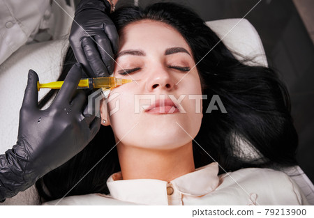 Brunette girl in cosmetology office during plasmolifting procedure lying with closed eyes 79213900