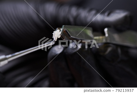 Steel dental forceps with ceramic bracket and a hand with a tiny colorful brush 79213937