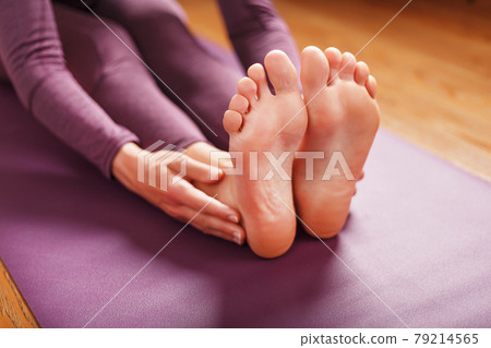 A woman lays out a lilac yoga mat on the wooden floor. A woman lays out a lilac yoga mat on the wooden floor. 79214565