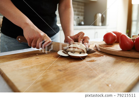 Close-up of chef or housewife hands while slicing mushrooms on a wooden kitchen board Close-up of chef or housewife hands while slicing mushrooms on a wooden kitchen board 79215511
