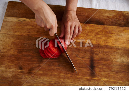 Top view of woman hand cutting tomato on a wooden board Top view of woman hand cutting tomato on a wooden board 79215512