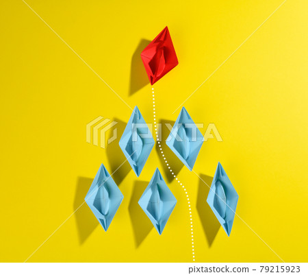 group of blue paper boats and one red led on a yellow background. group of blue paper boats and one red led on a yellow background. 79215923